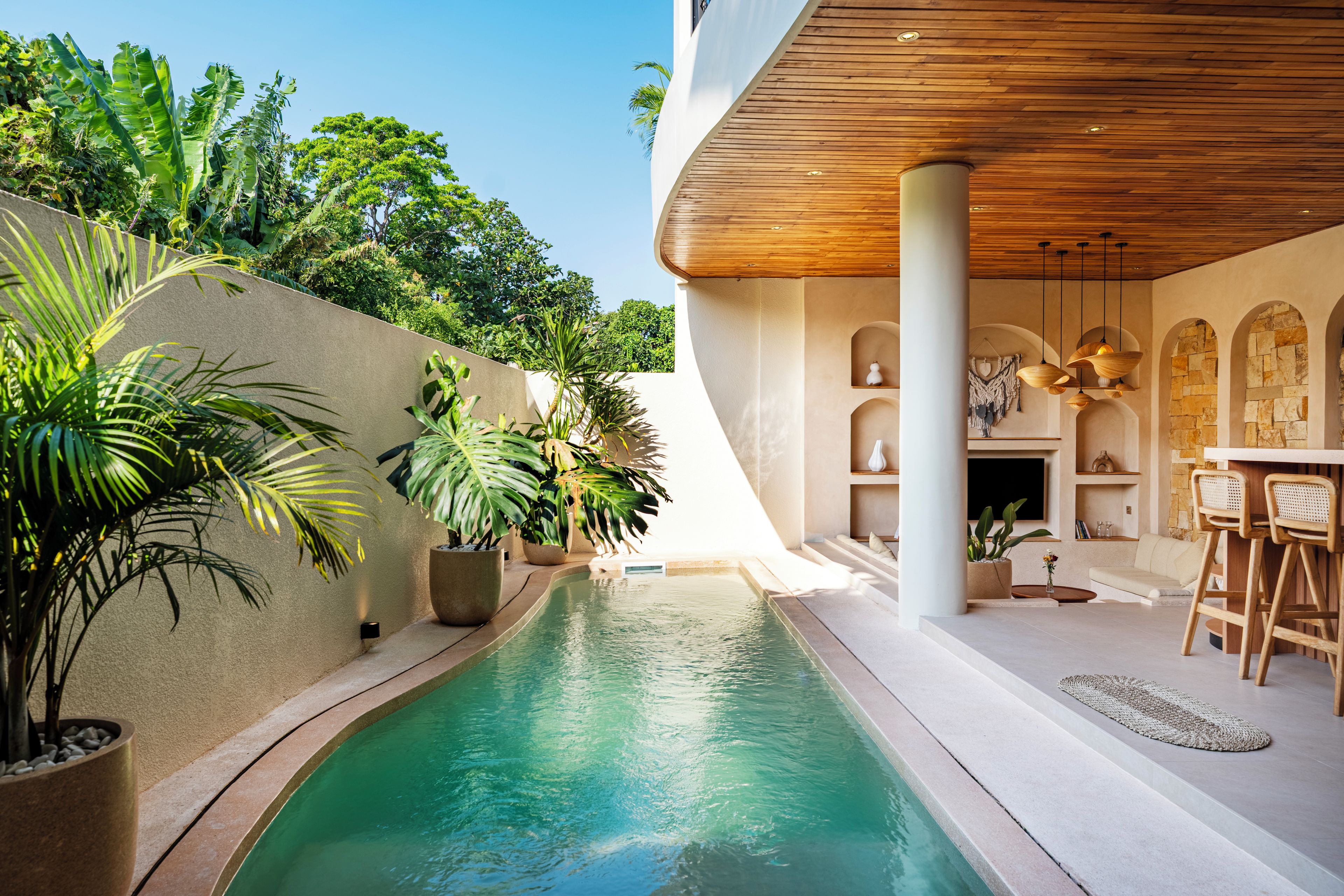 A modern pool area with a clear pool, surrounded by lush greenery and a wooden ceiling.