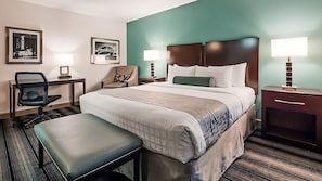 Quarto de hotel com cama, escrivaninha, cadeira, banco e duas luminárias de cabeceira.