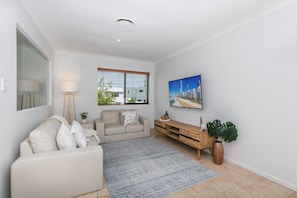 Ein modernes Wohnzimmer mit einer Couch, einem Couchtisch, einem Fernseher und einem großen Fenster mit Jalousien.
