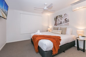 Ein Schlafzimmer mit einem Bett, einem Deckenventilator, einem an der Wand befestigten Fernseher und einem Gemälde.