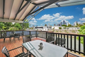 A deck with outdoor furniture, a table, and chairs, overlooking a river and city skyline. - BREEZE AT BROADBEACH - Elite Holiday Homes (Gold Coast)