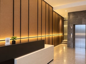 A modern reception area with a black reception desk, a QR code sign, and a potted plant. - Muraku Mega Kuningan Jakarta (Jakarta)