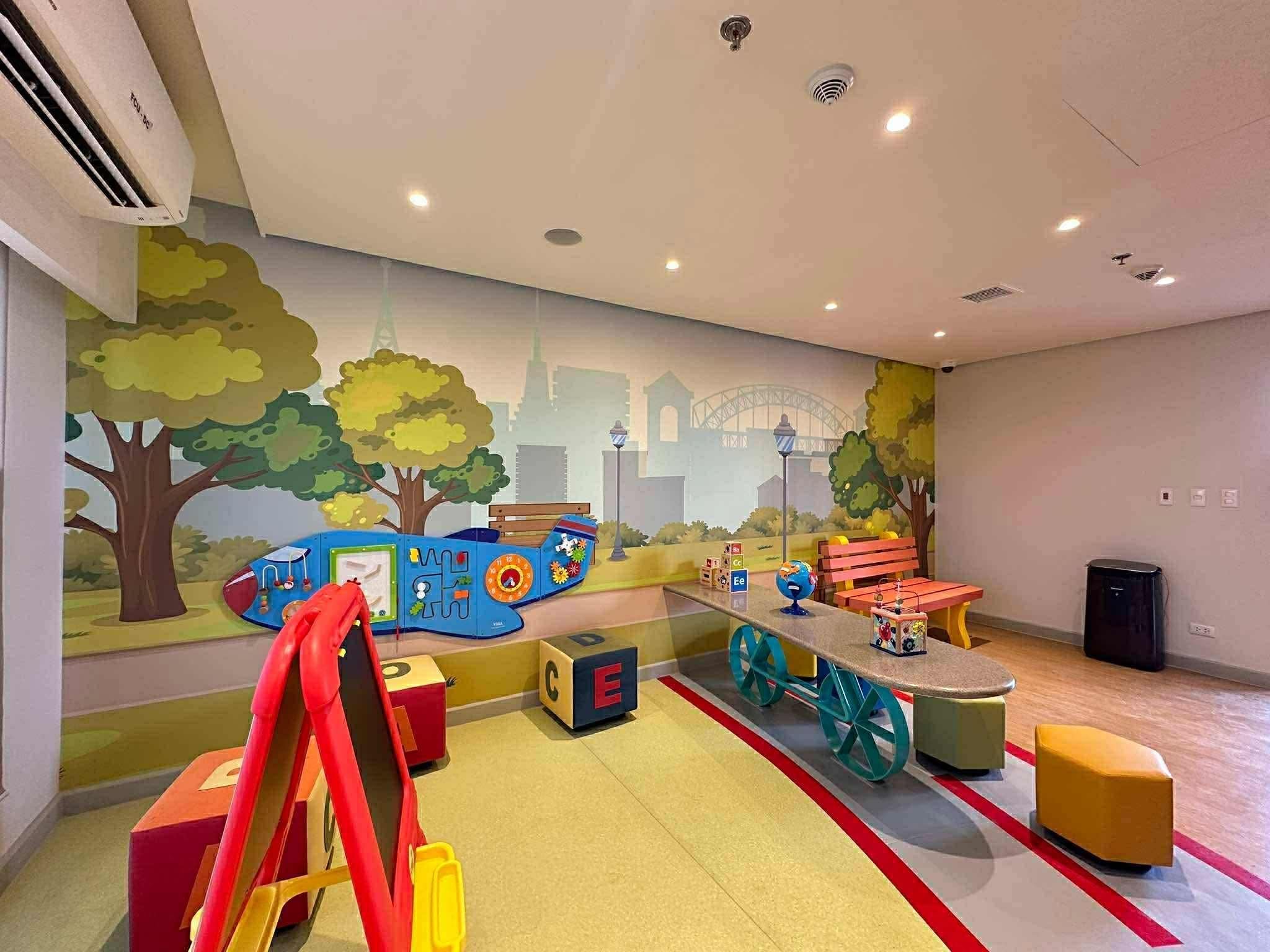 Un espace de jeux pour enfants agrémenté d’une fresque murale, d’aires de jeux et de sièges.