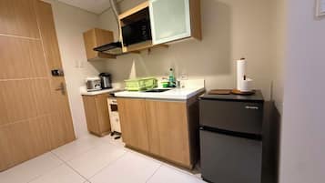 Una cocina compacta con armarios de madera, microondas integrado, pileta y heladera pequeña.