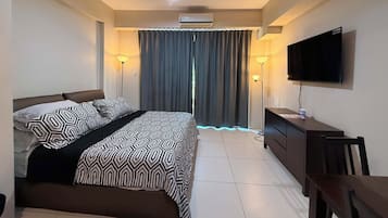 Una habitación de hotel con cama, escritorio, televisión y ventana con cortinas.