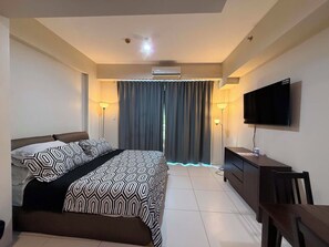 A hotel room with a bed, a desk, a TV, and a window with curtains. - Serene 1-bedroom condo with AC inside Pico De Loro Resort (Nasugbu)