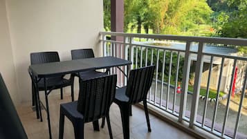Un balcón con una mesa y sillas, barandilla blanca y vistas a zonas verdes y una calle.