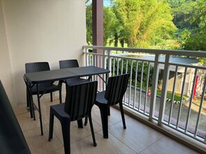 A balcony with a table and chairs, a white railing, and a view of greenery and a street. - Serene 1-bedroom condo with AC inside Pico De Loro Resort (Nasugbu)