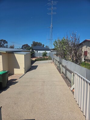 A clear pathway leading to a building with a corrugated metal fence on one side and a utility pole with antennas on the other. - Coastal Holiday Shack in Port Hughes/Moonta Bay with Boat parking and fire pit (Moonta Bay)