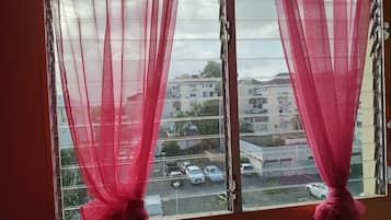 Una ventana con cortinas traslúcidas y vista a un estacionamiento y edificios.