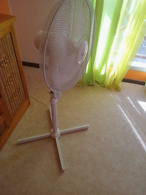 Un ventilador de peu amb una protecció de malla i un panell de control, col·locat sobre un terra amb moqueta.