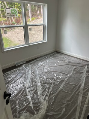 A room with a large window, plastic sheeting on the floor, and a door with a black handle.