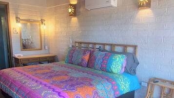 A room with a bed, a bench, a wall-mounted air conditioner, and a brick wall.