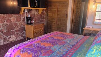 A room with a bed, a TV, a coffee machine, and a wooden shelf.