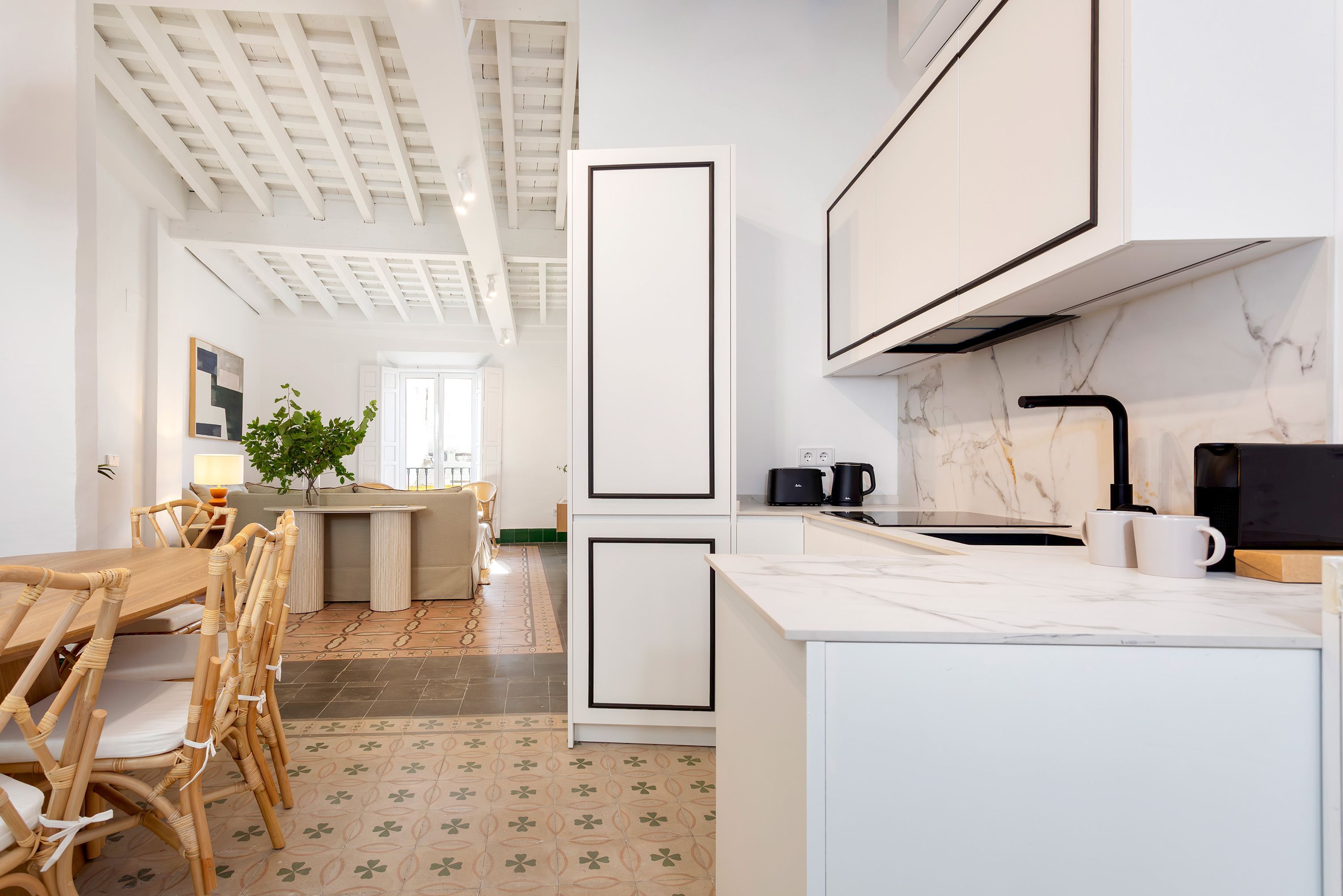 A modern kitchen with white cabinetry, a marble countertop, and a dining area with a wooden table and chairs.