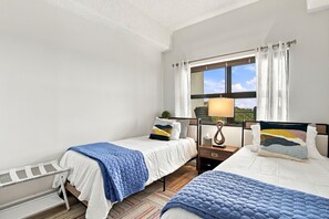 Una camera d'albergo con due letti, una finestra con tende, un comodino con lampada e vista sull'esterno.