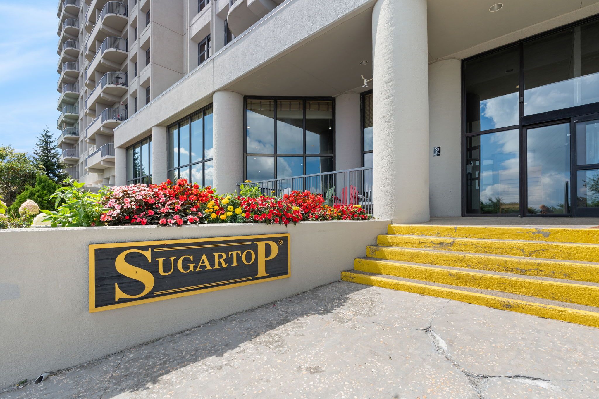 A hotel entrance with a sign reading 'Sugartop' and a set of yellow steps leading up to the entrance.