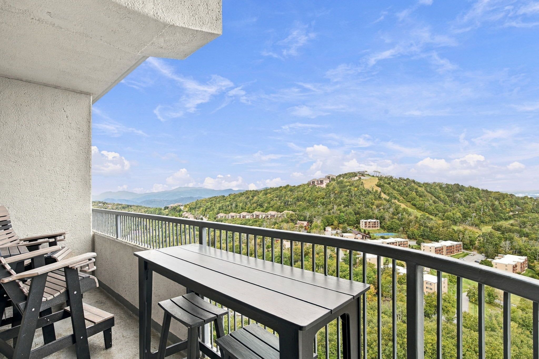 Un balcon avec une table et des chaises, donnant sur une colline parsemée de bâtiments et de verdure.