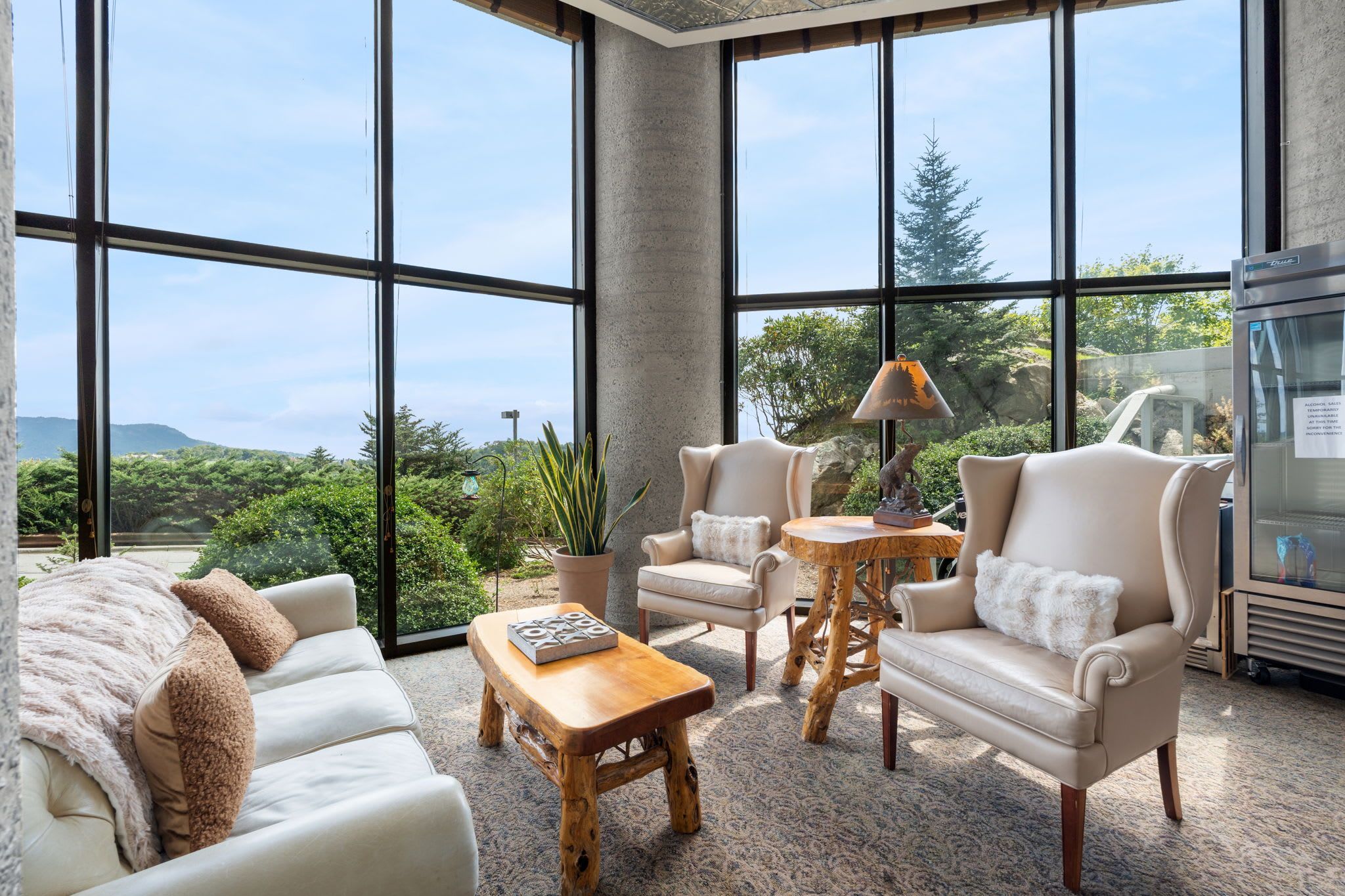 A spacious living room with large windows, a sofa, two armchairs, a coffee table, and a lamp.