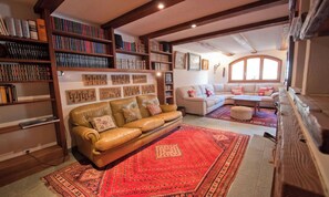 Ein gemütliches Wohnzimmer mit einem Ledersofa, einem roten Teppich mit Muster und Bücherregalen voller Bücher.