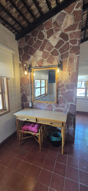 Quarto com parede de pedra, toucador de madeira e janela.