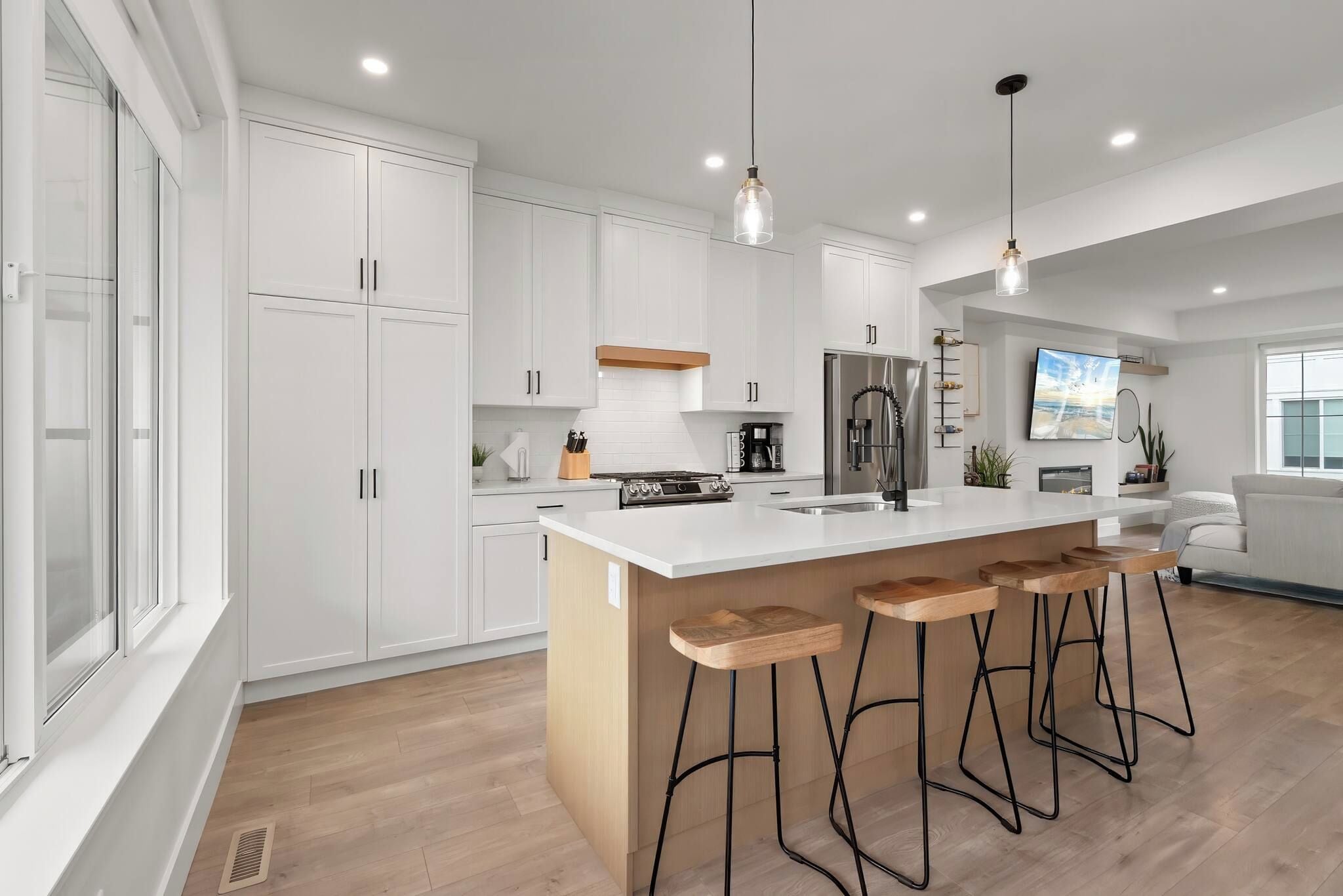 A modern kitchen with white cabinetry, a central island with stools, a built-in oven, and a stainless steel refrigerator.