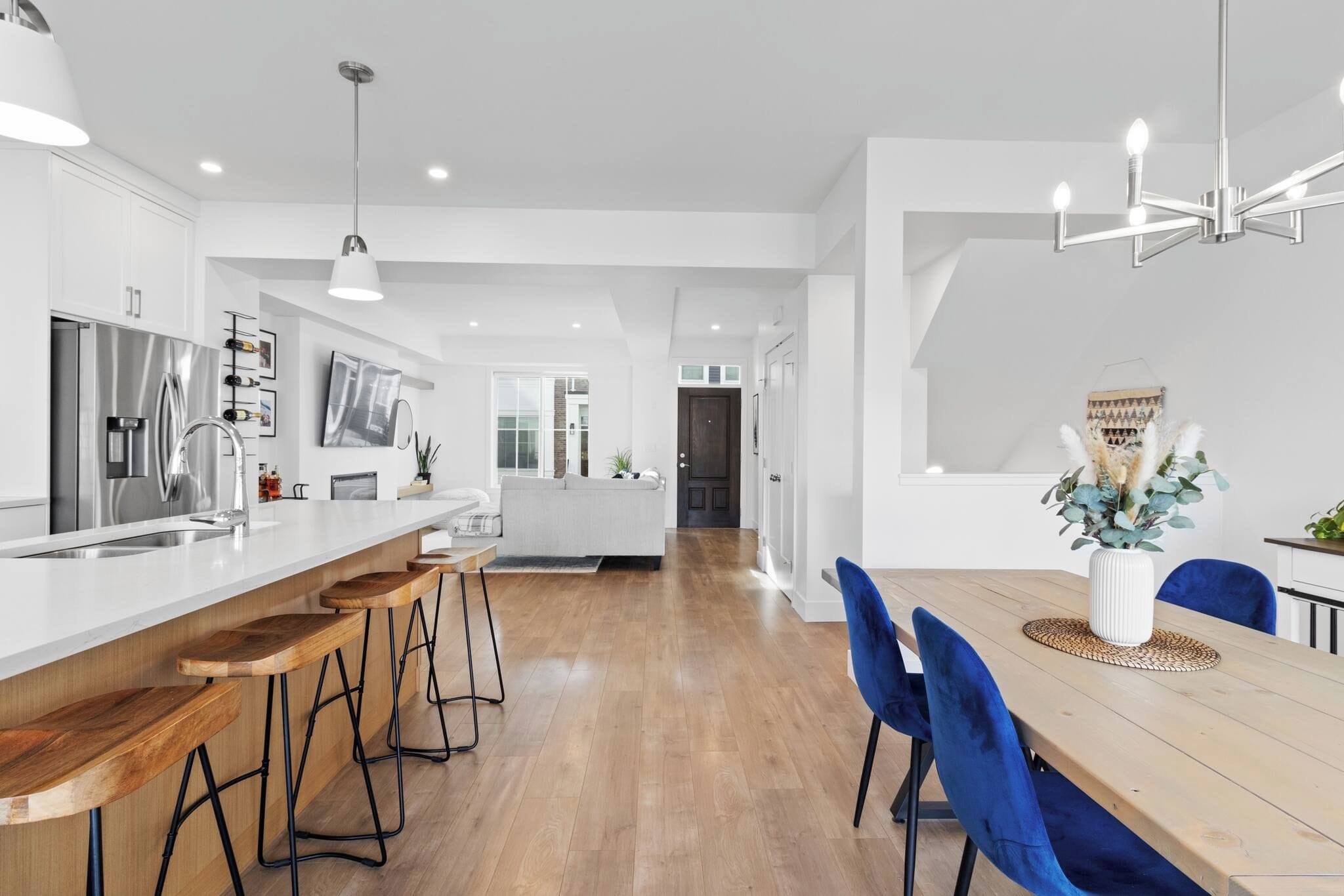 A modern kitchen with a central island, bar stools, and a dining area with a wooden table and blue chairs.