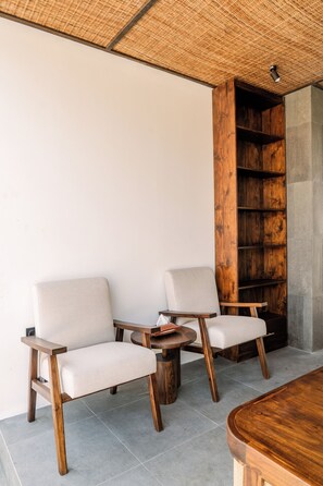 Een modern interieur met twee gestoffeerde fauteuils, een ronde houten tafel en een ingebouwde houten boekenkast.