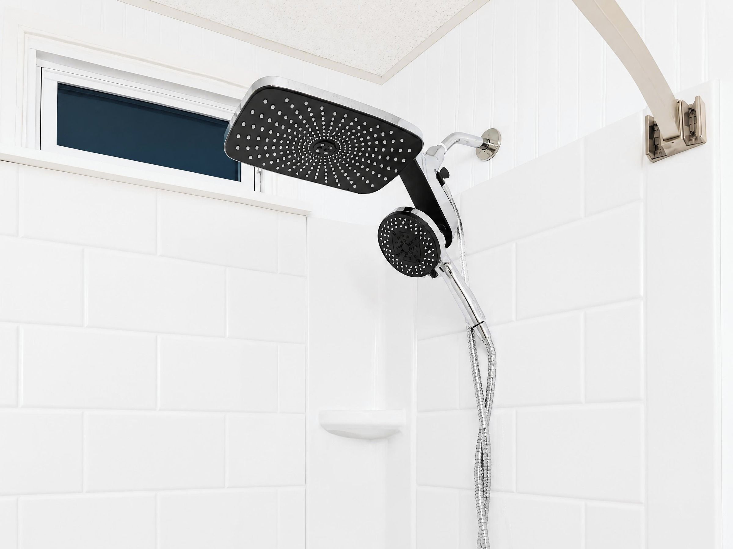 Eine Dusche mit Handbrause und Deckenbrause, beide in Schwarz und Silber gehalten, an einer weiß gefliesten Wand angebracht.