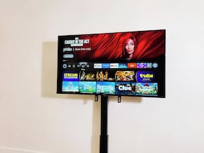 Et fladskærms-tv på væggen viser en streamingtjenestes brugerflade med forskellige indholdsvalg.