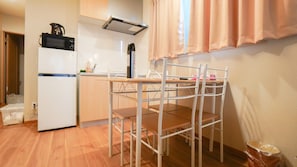 Eine Küchenzeile mit Mikrowelle, kleinem Kühlschrank und Spüle. Ein Stuhl mit Metallgestell und ein Tisch sind ebenfalls vorhanden.