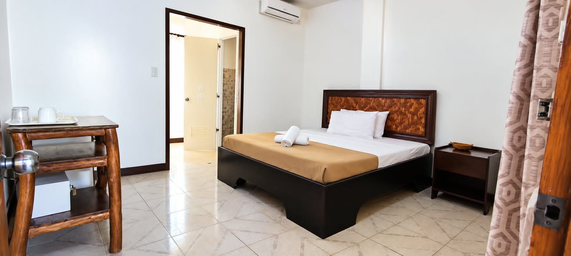 A hotel room with a bed, bedside table, and a wooden side table with a tray.
