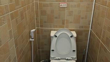 A small, tiled bathroom with a toilet, a hand dryer, and a warning sign on the wall.