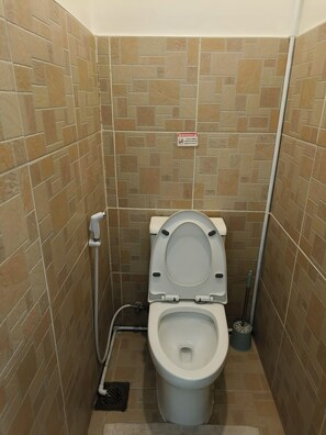 Ein kleines Badezimmer mit Fliesen, einer Toilette, einem Händetrockner und einem Warnschild an der Wand.