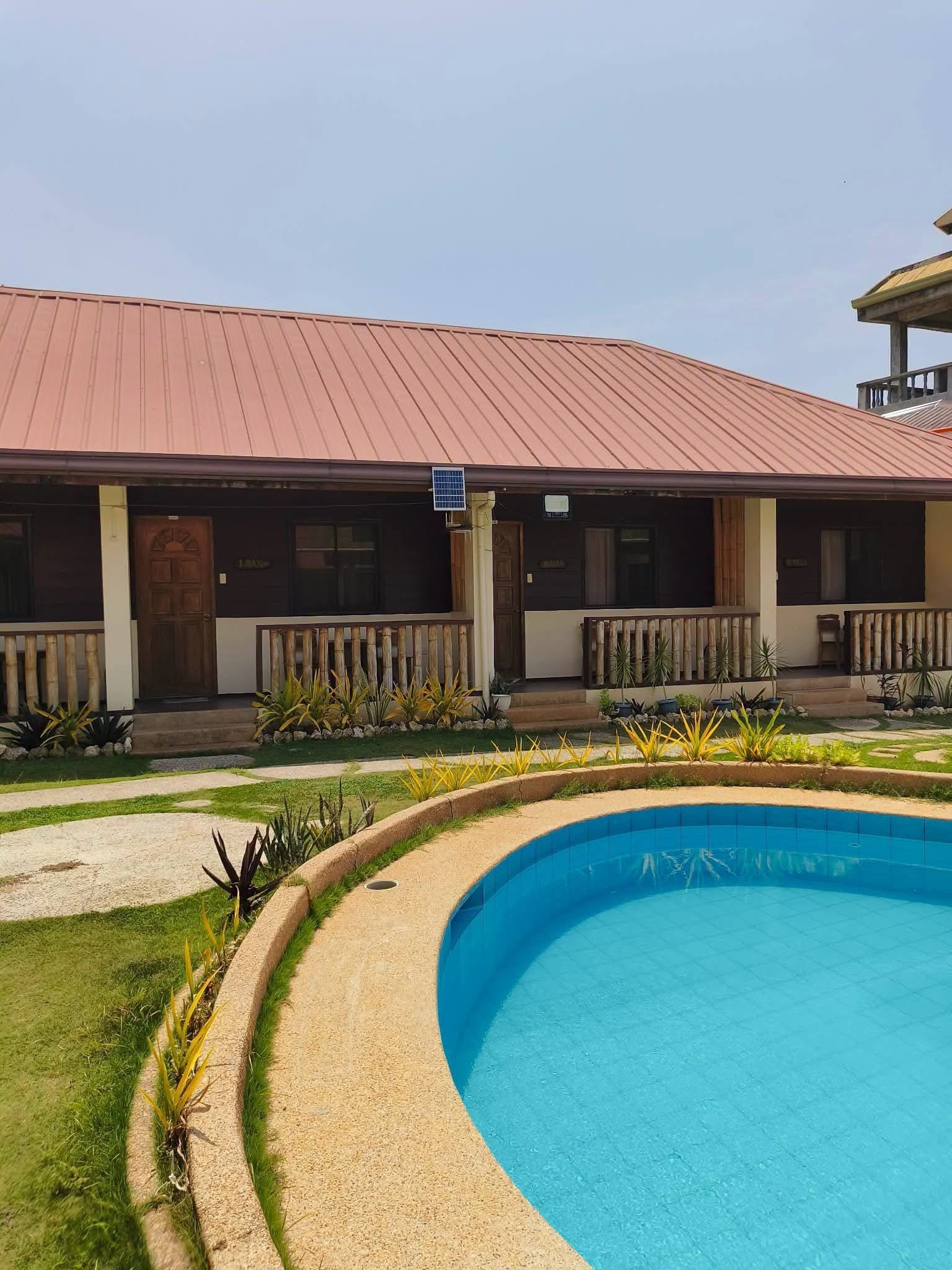 A hotel with a swimming pool, a covered outdoor area, and a building with a red roof.
