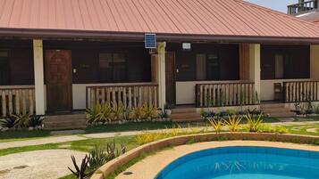 A hotel with a swimming pool, a covered outdoor area, and a building with a red roof.