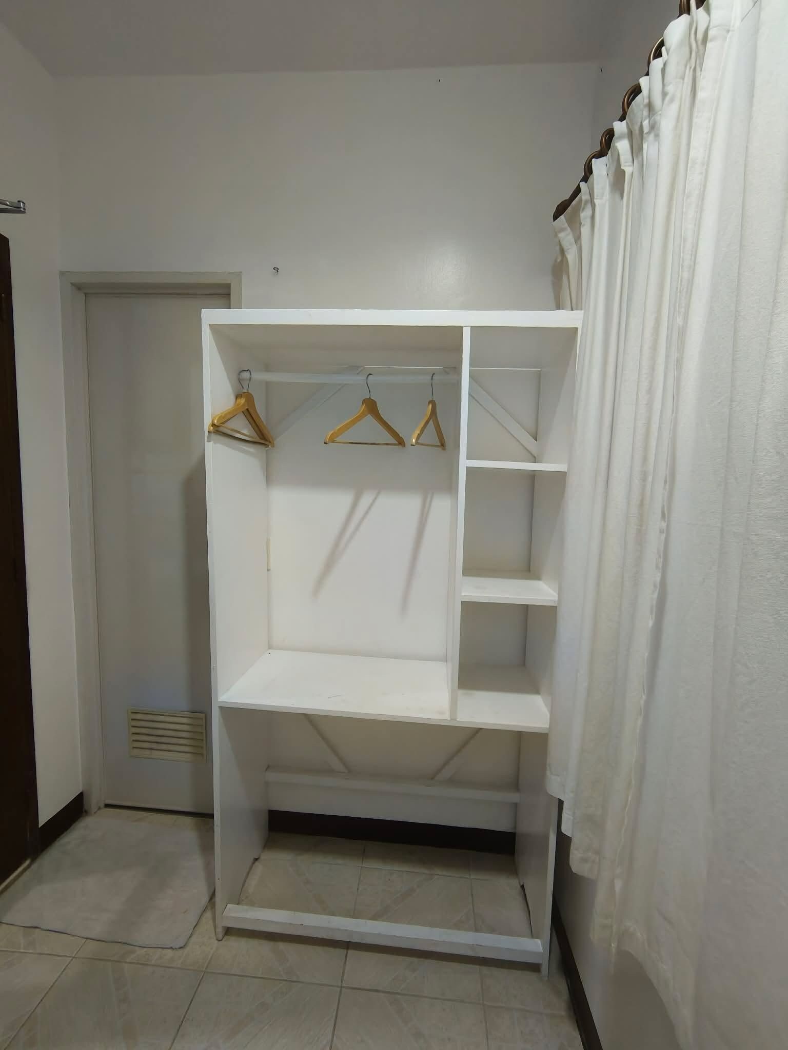 A white closet with multiple shelves and hanging space, located in a room with a tiled floor and a door in the background.