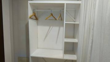Un armario blanco con varios estantes y espacio para colgar ropa, situado en una habitación con suelo de baldosas y una puerta al fondo.
