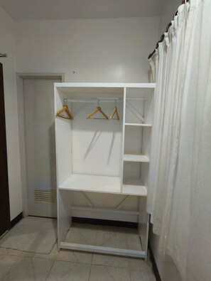 Ein weißer Kleiderschrank mit mehreren Regalen und Ablageflächen, befindet sich in einem Raum mit gefliestem Boden und einer Tür im Hintergrund.