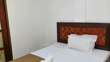 Una cama bien hecha con ropa blanca y una colcha marrón, un cabecero de madera y un equipo de aire acondicionado en la pared.