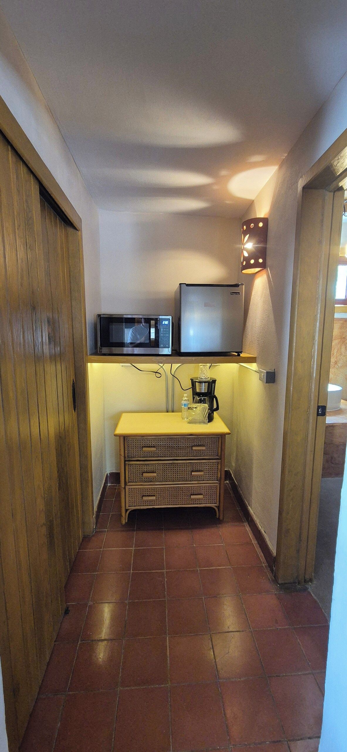 Une cuisine compacte équipée d’un four à micro-ondes, d’un réfrigérateur et d’une machine à café, le tout installé sur un plan de travail en bois.