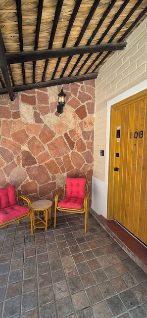Área de estar coberta ao ar livre, com paredes de pedra e porta de madeira com a inscrição '10B'.