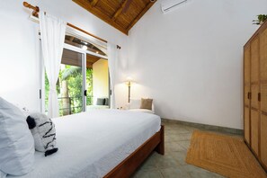 Ein Schlafzimmer mit Bett, Nachttisch, Lampe, Kleiderschrank und Blick auf Grünflächen.