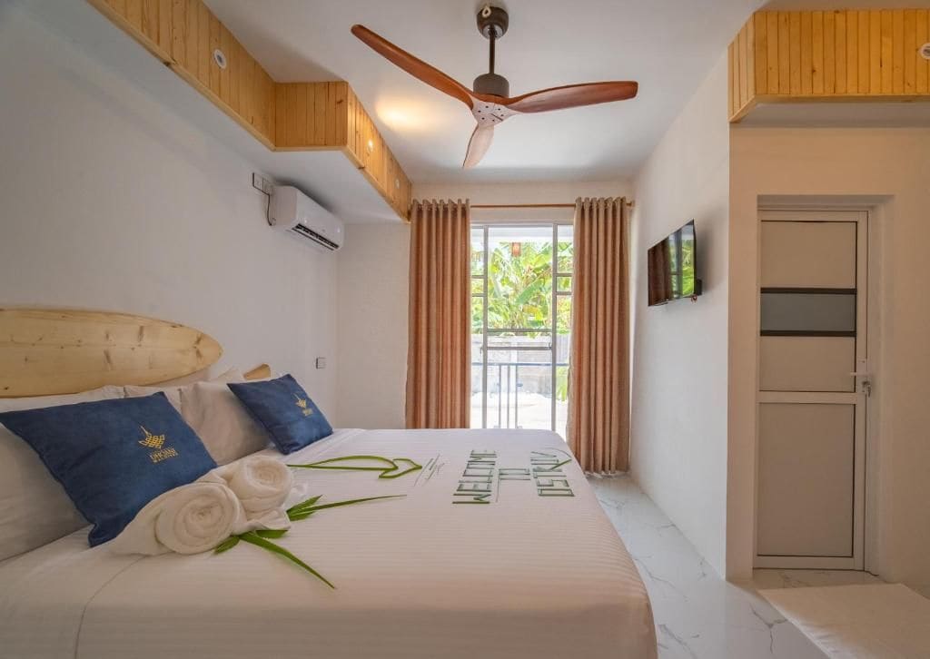 A hotel room with a bed, a ceiling fan, a TV, and a window with curtains.