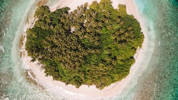 An aerial view of a tropical island with a central forested area surrounded by a sandy beach and clear turquoise waters.