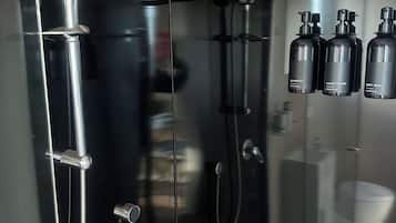 Une salle de bain moderne avec une douche à parois de verre, un pommeau de douche à main, un robinet mural et trois flacons de produits de toilette fixés au mur.