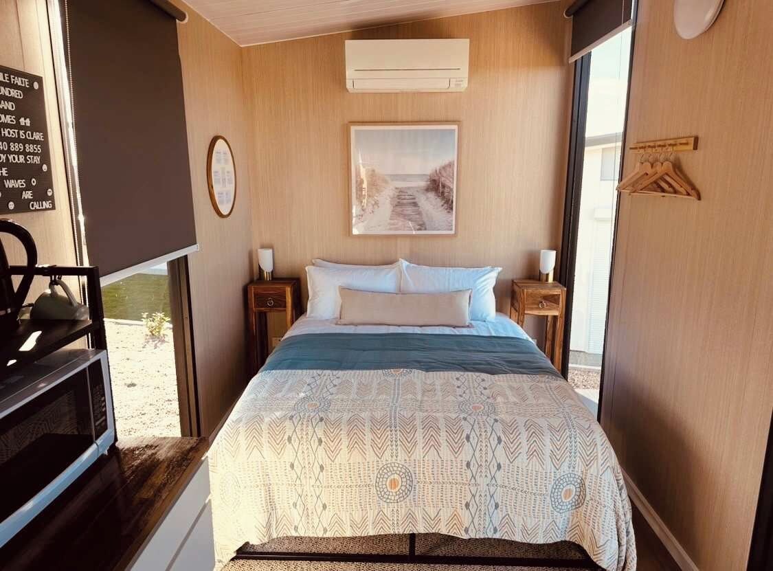 Ein Schlafzimmer mit einem Bett, einem Nachttisch, einer Wand-Klimaanlage, einem gerahmten Bild und einer Holztür.