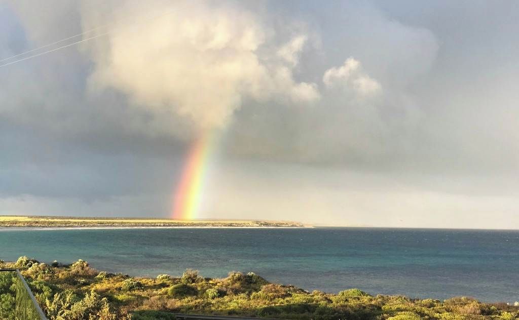 Eine Küstenlandschaft mit Regenbogen, einem Gewässer und einer fernen Landmasse.