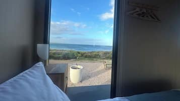 Ein Zimmer mit einem Bett, einem Fenster mit Meerblick und einem kleinen Tisch mit einer Topfpflanze.