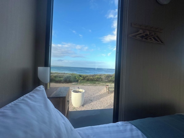 A room with a bed, a window with a view of the sea, and a small table with a potted plant.